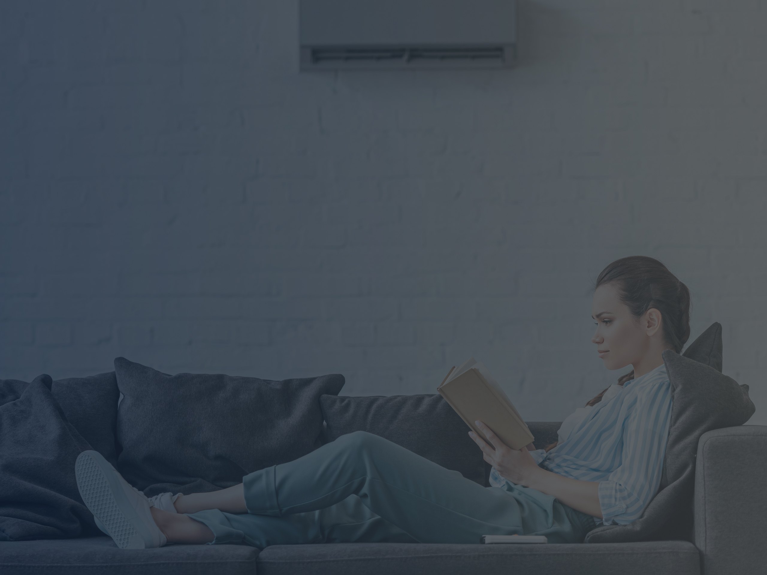 Woman Reading a Book on a Sofa with Wall Air Conditioner On