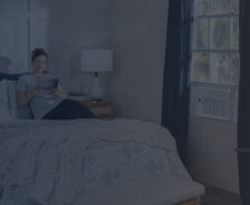 Woman in Bedroom Reading Book with Window AC Turned On