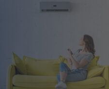 Young Woman Sitting on Yellow Sofa under Air Conditioner at Home